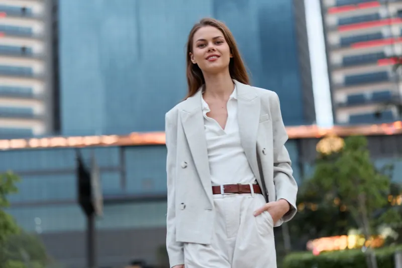 confident woman in white business suit posing outdoors with urban office building background, smiling, professional fashion style, spring season