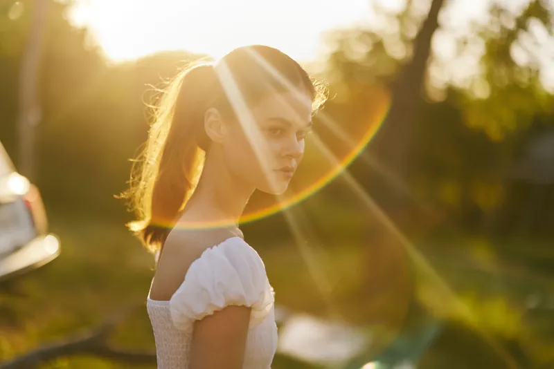 Young woman in a white dress enjoying a sunny afternoon, captured in warm golden light with a serene expression Perfect for themes of nature and tranquility