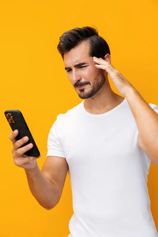 Мужчина с улыбкой держит смартфон, стоя в жёлтой студии
