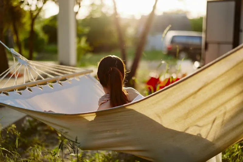 A contemplative young woman enjoying a serene moment in a hammock at sunset, surrounded by lush greenery, embodying peace and relaxation