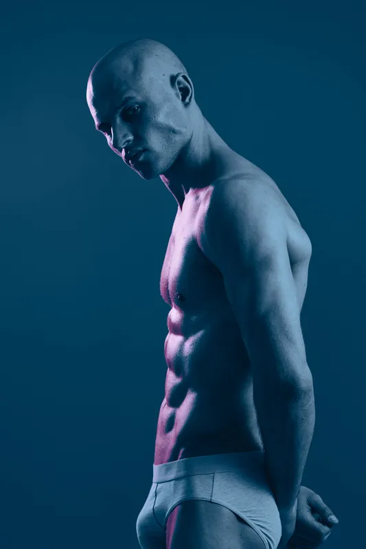Athletic man posing in a striking blue light, showcasing muscular definition and a powerful physique in a captivating black and white style.