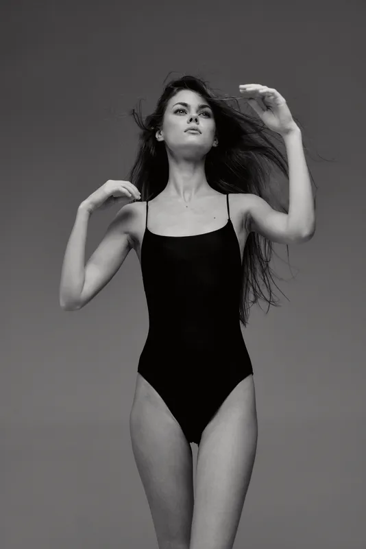 Black and white portrait of a woman in a black swimsuit posing with flowing hair and confident expression