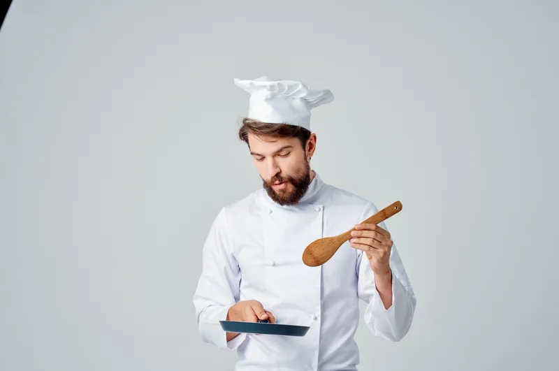 Повар-мужчина держит сковороду в руке, готовит еду, гурманская кухня, светлый фон