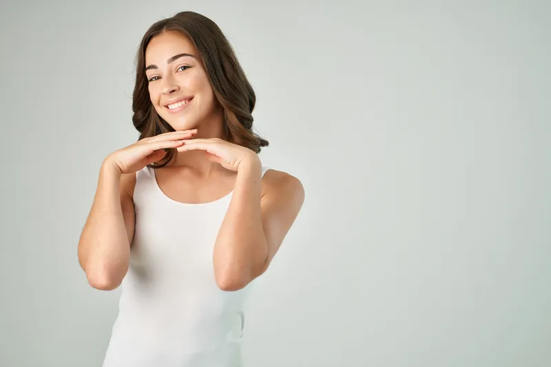 Жизнерадостная женщина в белой футболке с красивыми волосами улыбается и позирует