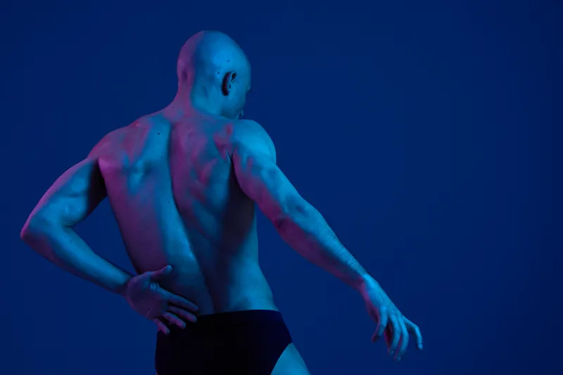 Dynamic man with a striking pose, showcasing fitness and strength against a stunning blue and purple background in a captivating black and white image.