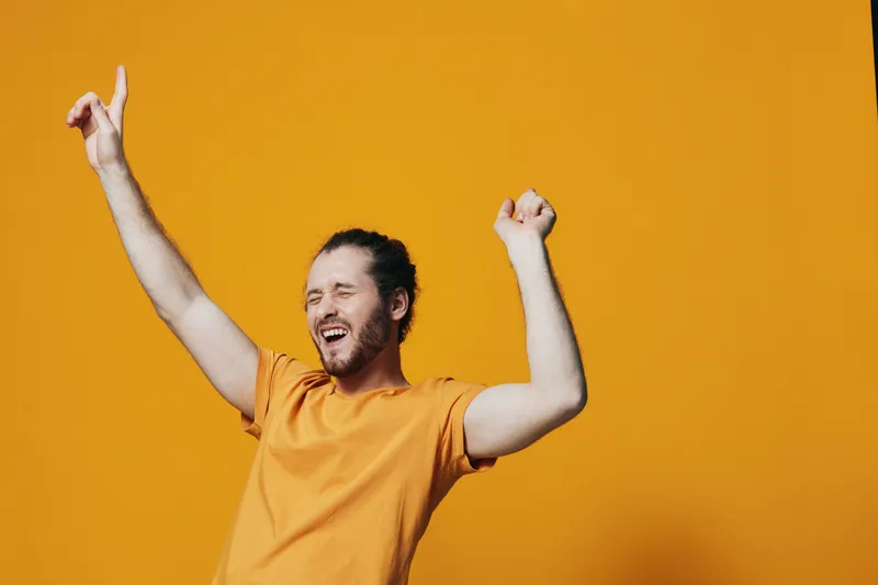 Happy young man celebrating joyfully against a vibrant orange background, wearing a casual orange t shirt, exuding excitement and positivity