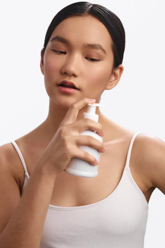 asian woman in a bright studio applies skincare product using a spray bottle on her face, conveying a calm beauty routine and contemporary self care.