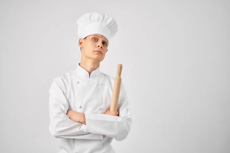 Шеф-повар в колпаке с кухонной утварью работает на кухне