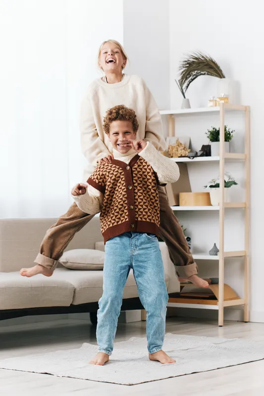 Joyful mother lifts child in a bright living room, capturing a playful moment of laughter and strong family bond in a cozy, sunlit home setting.