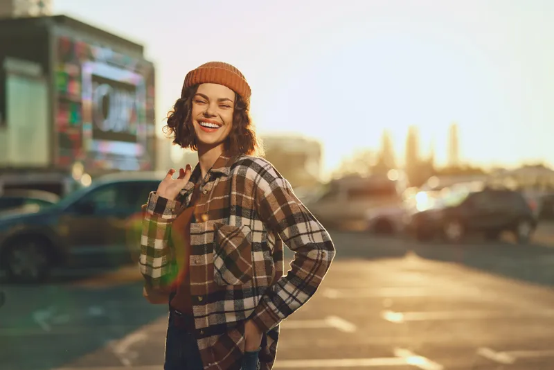 Woman smile urban beanie plaid golden glow candid portrait of a young woman at sunset, authenticity and mindful lifestyle vibe with emotional storytelling atmosphere in city street.