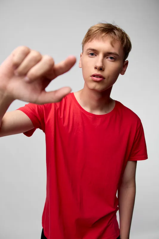 Thumbs down gesture from a young man in a red shirt, disapproval evident in a front view under studio lighting, suitable for evaluation, feedback or rejection scenes