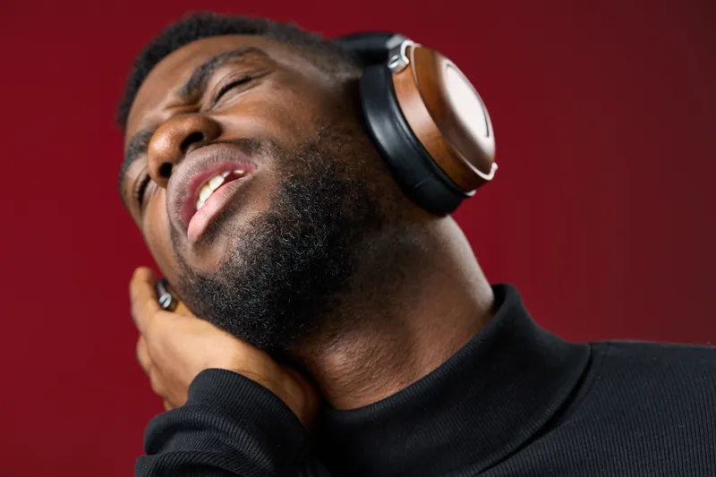 A joyful Black man listening to music with headphones, expressing deep emotion against a rich red background, showcasing relaxation and enjoyment in a contemporary style