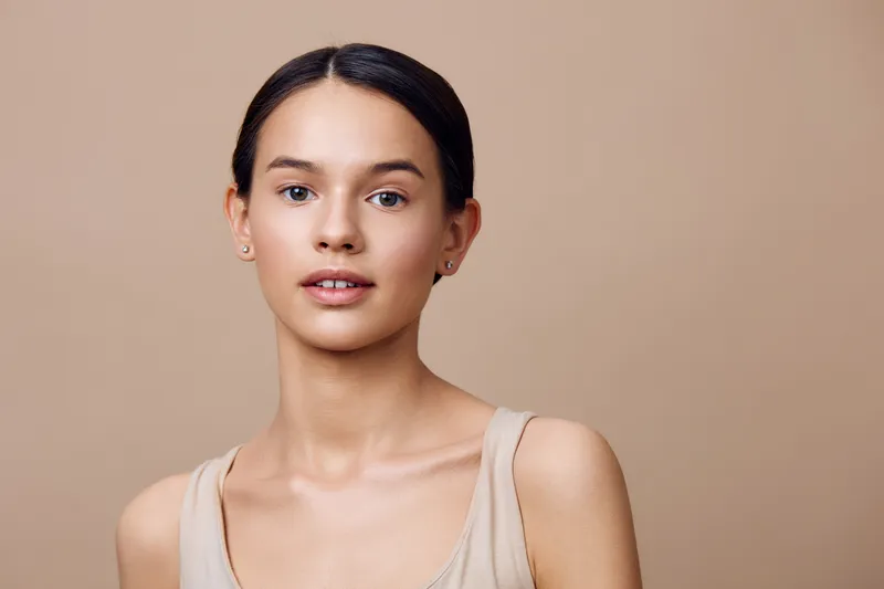 Young woman with natural makeup and a neutral background, expressing confidence and serenity, ideal for beauty and skincare concepts