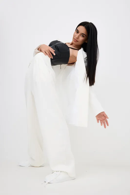 young woman in black corset and white wide pants posing gracefully on white background, modern fashion style, long dark hair, studio portrait