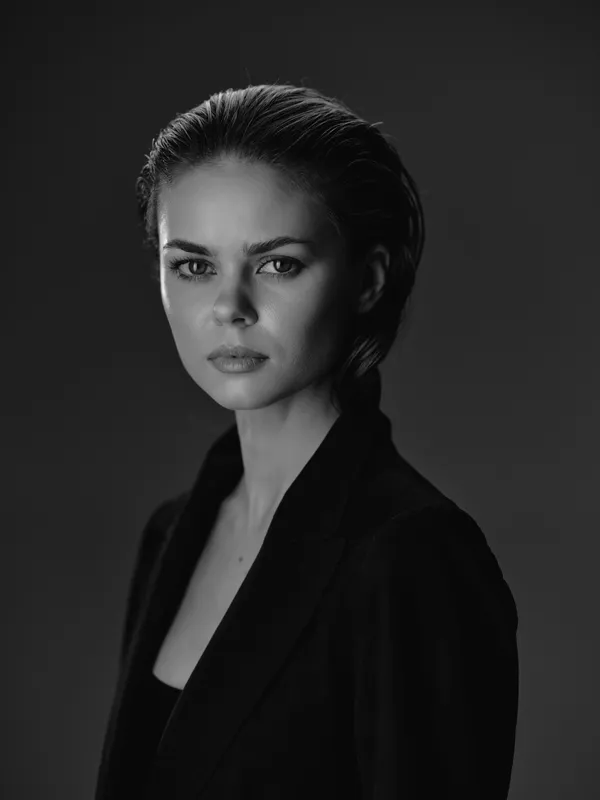 Black and white portrait of a serious woman with short hair wearing a dark blazer against a dark background.