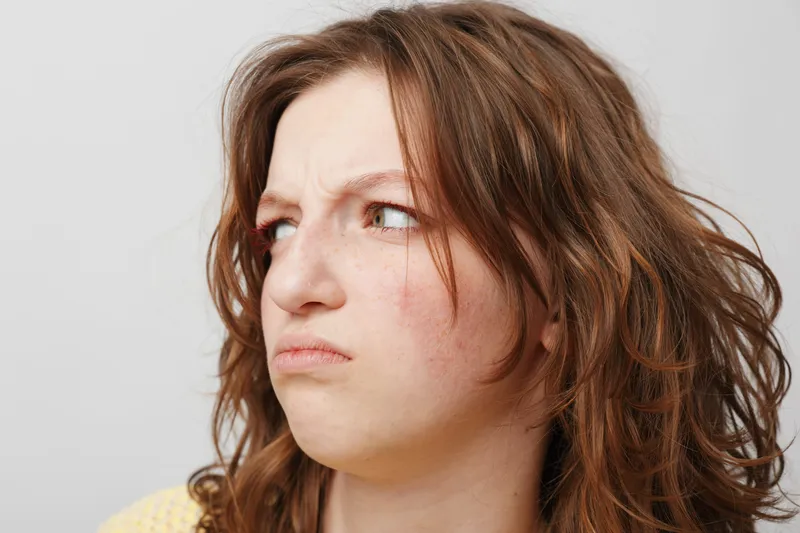 Close-up of a young woman with red hair showing a displeased facial expression, looking sideways. Concept of dissatisfaction, annoyance, and negative emotions in casual portrait.