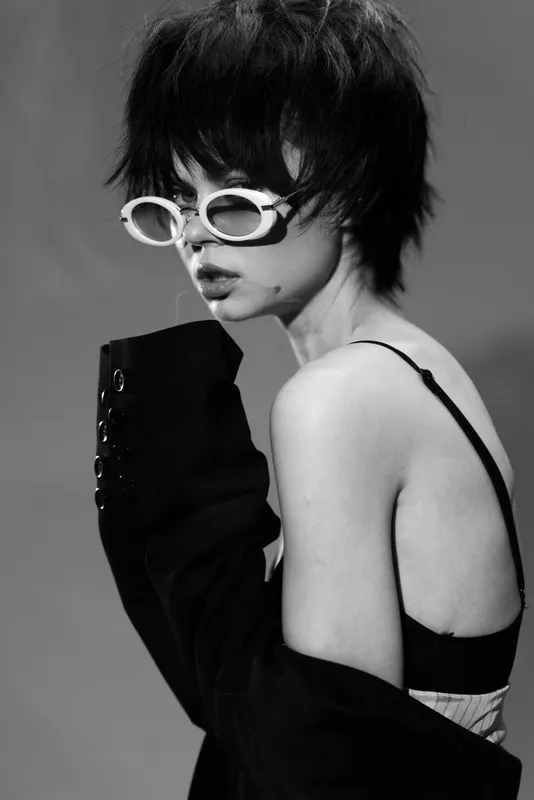 Black and white portrait of a young woman with short hair wearing sunglasses and a dark jacket, showcasing edgy fashion style.