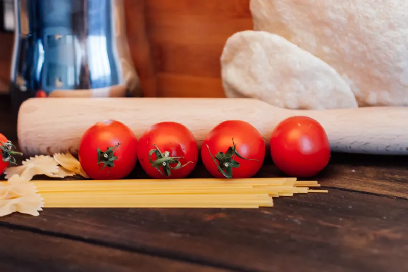 Приготовление итальянской кухни: мука и продукты на кухонном столе с помидорами черри