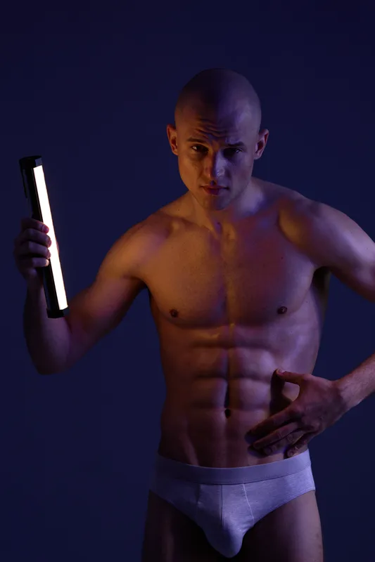 Strong man posing with a light source in a dramatic black and white image, showcasing physical strength and confidence, emphasizing muscle definition and expression.