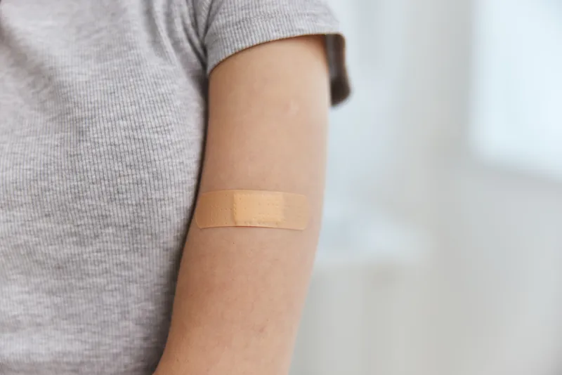 На плече наклеен пластырь, символизирующий вакцинацию, паспорт здоровья, иммунитет и больницу