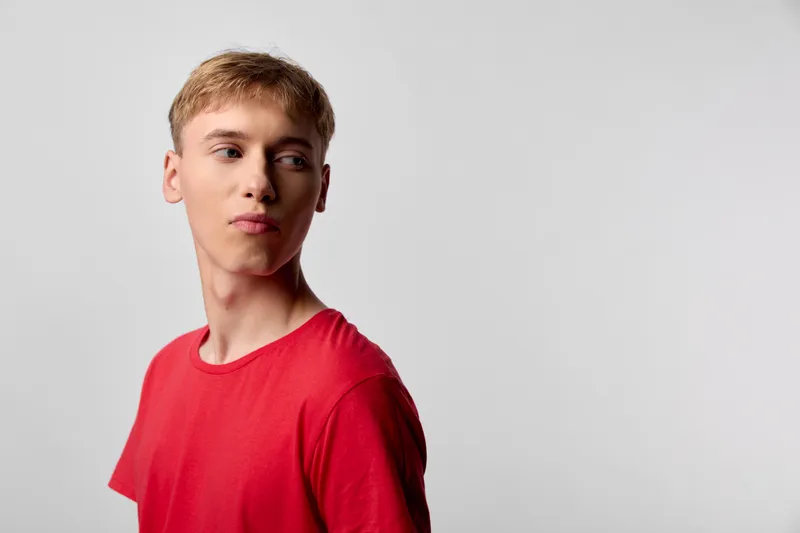 Young man in a red shirt appears in side profile against a neutral studio background, captured with clean studio lighting, fashion photography vibe, and a calm contemplative mood for modern style and