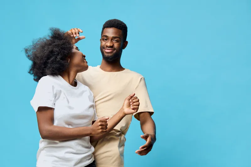 Happy couple dancing together against a bright blue background, showcasing joy and connection with casual summer attire, perfect for relationship and lifestyle themes