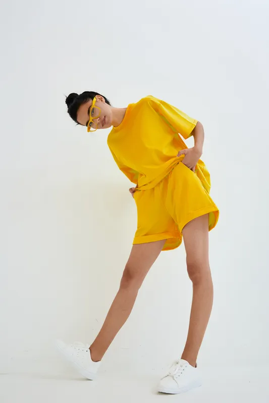 young woman in yellow casual outfit with shorts and sunglasses posing on white studio background, modern style and minimalistic look with dynamic posture