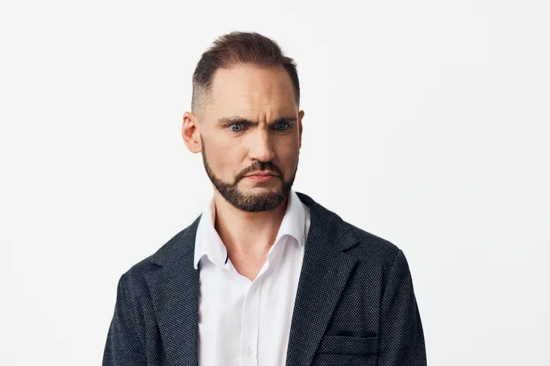 An isolated colored background frames a business professional man, conveying focus and wary confidence as he analyzes a task, with a stern yet controlled expression and an intent gaze.
