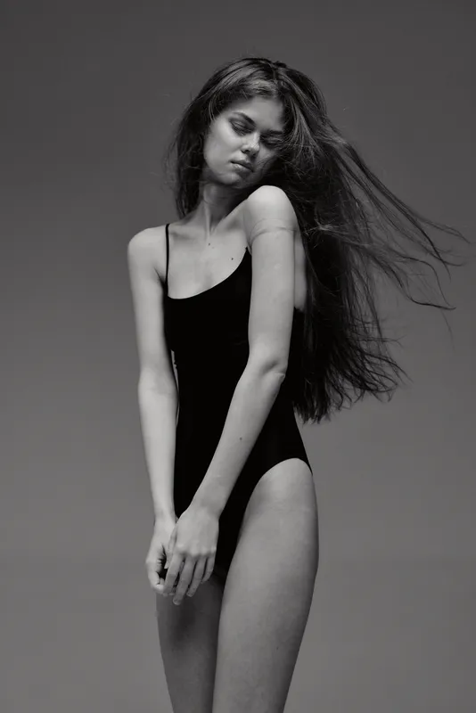 Black and white portrait of a young woman in a black swimsuit with flowing hair and a neutral expression