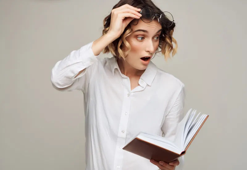 Женщина с кудрявыми волосами в очках держит в руках книгу, работая в студии