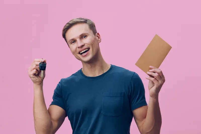 smiling young man hold car key and envelope isolated pink background happy cheerful casual style concept digital nomad technology finance investment