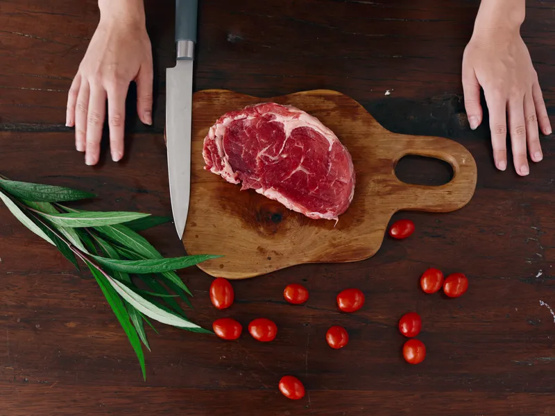 Женщина с ножом в руке нарезает свежее мясо для жарки на кухне