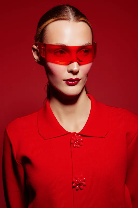 Portrait of a woman wearing red sunglasses and a red sweater against a red background. Fashion concept with bold colors and modern style emphasizing confidence and elegance.