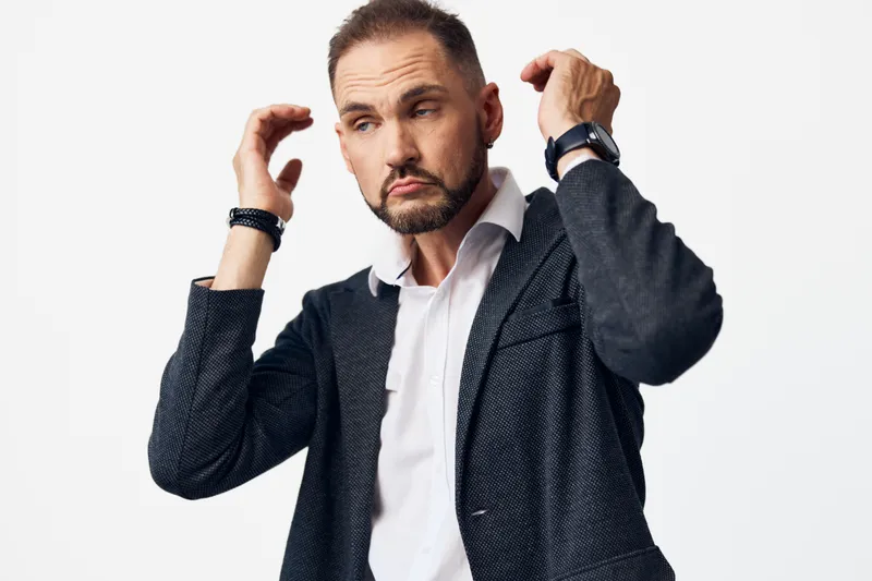Professional man on an isolated colored background, showing doubt and focus. He adjusts his blazer and hair, conveying concentration, seriousness, and quiet tension in a corporate scene.