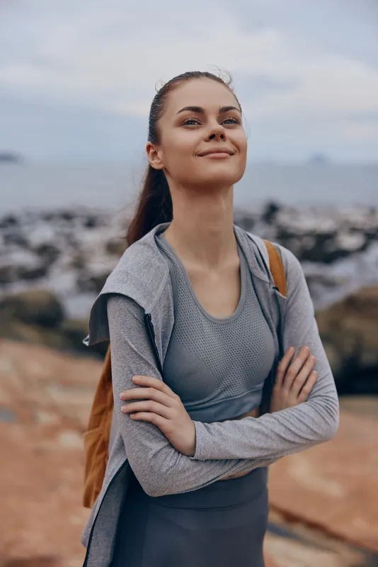 Young woman in sportswear enjoying nature with a calm expression, set against a coastal backdrop, embodying motivation and wellness in an outdoor setting