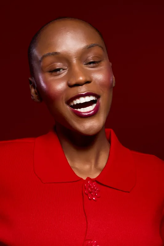 Close-up of happy African woman with dark skin laughing, wearing red sweater against dark red background. Concept of joy, beauty, fashion, and confident female model with natural look.