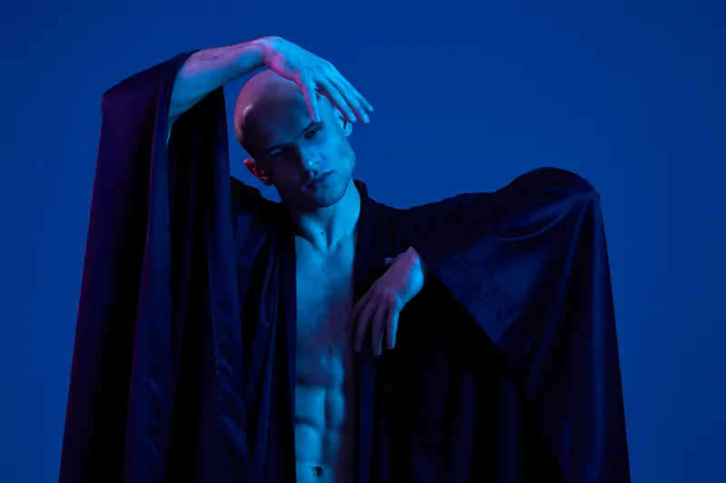 Artistic and captivating image of a man in a flowing garment, showcasing expressive poses and dramatic lighting effects in shades of blue.