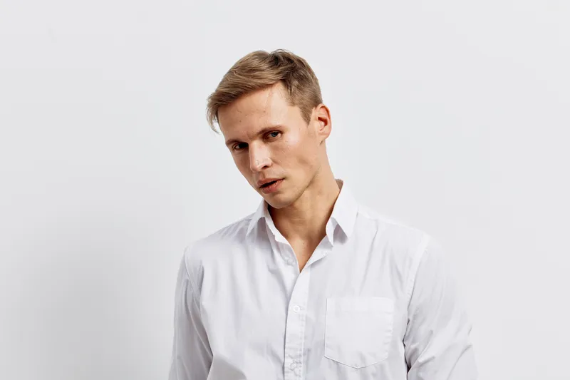 Confident young man with short hair wearing white shirt looking directly at camera isolated on plain light background studio portrait. People lifestyle concept, fashion, elegance, professionalism, nat