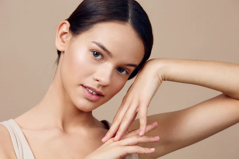 Portrait of a young female model with a calm expression, showcasing healthy skin tone and natural beauty, against a neutral background in soft colors
