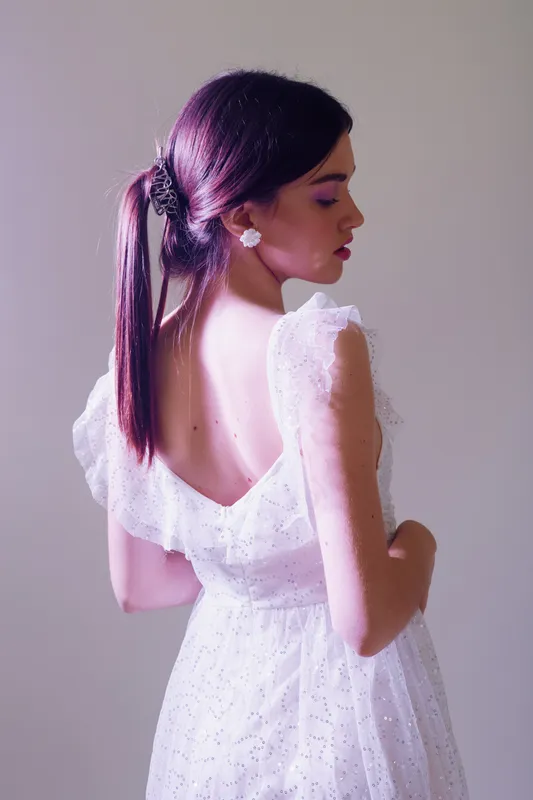 Young woman in a white dress with open back poses sideways against a plain background. Concept for beauty, fashion, elegance, and feminine style.