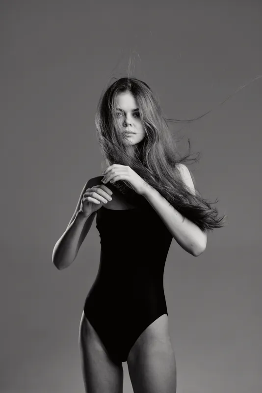 Black and white portrait of a young woman in a black bodysuit with flowing hair, showing a calm and introspective mood.