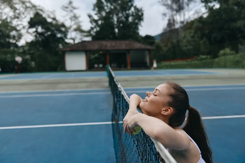 Young woman enjoying a moment of relaxation on a tennis court, wearing sporty attire, showcasing joy and tranquility in a vibrant outdoor setting