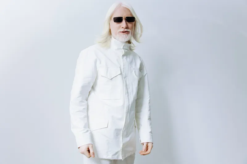 Модный пожилой мужчина с длинными седыми волосами и солнцезащитными очками одет в современную белую куртку