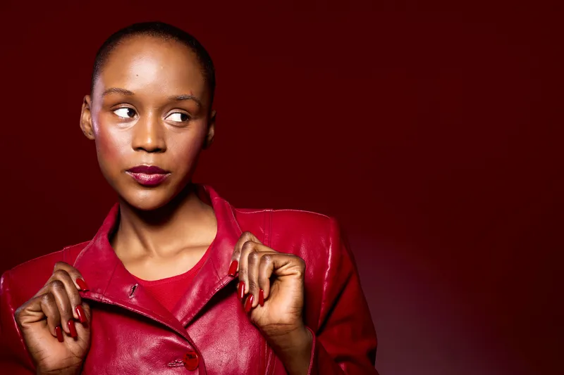 Portrait of a confident black woman with dark skin wearing a red leather jacket against a dark red background. Concept for fashion, style, and elegance with a bold color palette.
