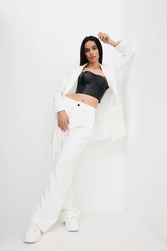 stylish woman wearing black crop top and white suit posing confidently in bright minimalist corner, modern fashion, casual elegance, monochrome outfit