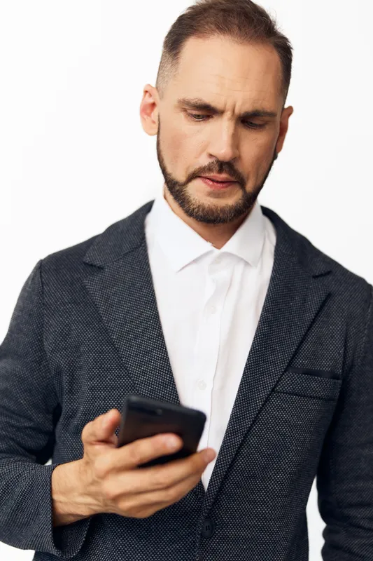 A professional man in business attire studies a mobile device against an isolated colored backdrop, showcasing focus, determination, and thoughtful mood in a clean corporate scene.