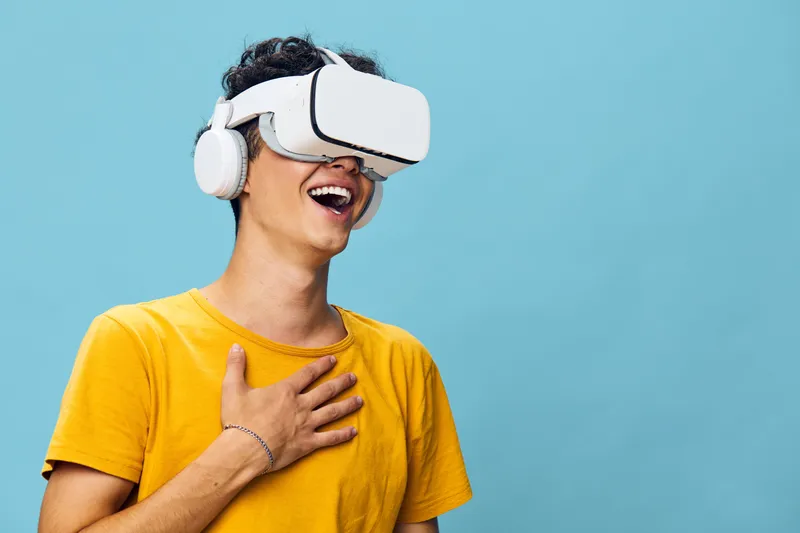 Счастливый молодой человек наслаждается опытом виртуальной реальности в VR-шлеме и наушниках, выражая радость и удивление
