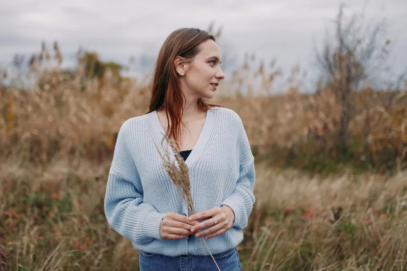 Young woman standing in a windswept meadow, captured in an authentic portrait conveying genuine calm and contemplative expression, natural light and realistic mood, soft tones