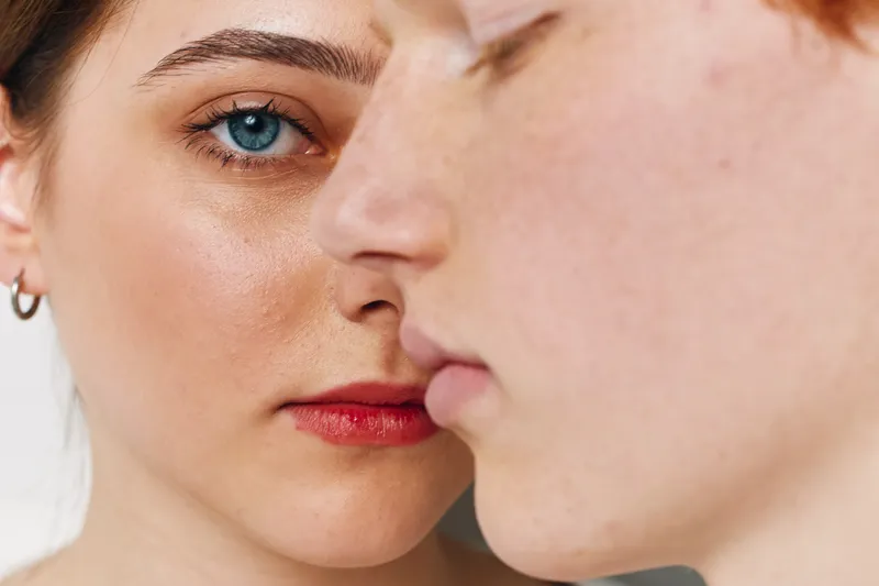 Closeup portrait of young woman and man with natural skin, blue eye, and serious expression in intimate composition on neutral background for beauty and emotions.