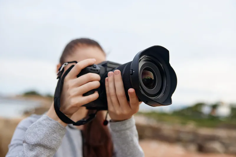 Young woman capturing scenic views with a professional camera, expressing creativity and enthusiasm in a natural outdoor setting, ideal for photography concepts and inspiration